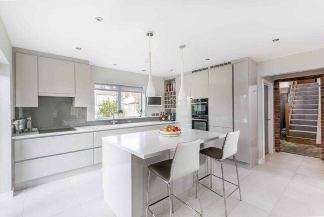 Modern white kitchen with a sleek built-in cooker hood hidden inside matching wall cabinets, creating a clean and uncluttered look.