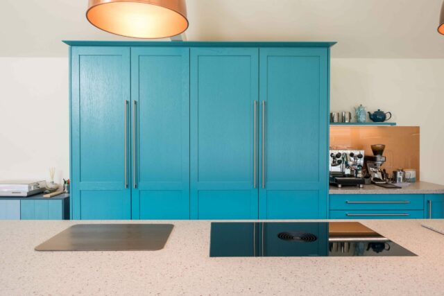 Bright kitchen with blue cabinets and a central island hob featuring a downdraft extractor, blending into the worktop for a minimalist finish.